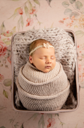 Newborn swaddled in knit layers in a vintage basket